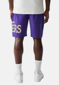 Pantaloni corti viola in cotone misto con testo giallo "Los Angeles Lakers". Presentano una vita elastica e una lunghezza sopra il ginocchio.
