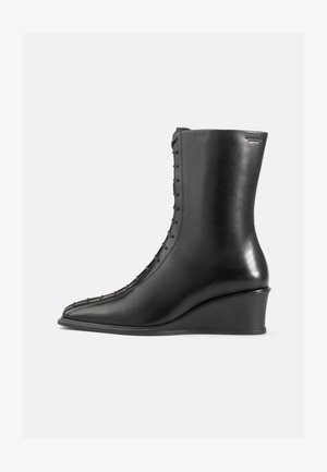 Black leather ankle boot with a wedge heel, featuring a pointed toe and a side lace-up design with stitched detailing. Smooth texture.