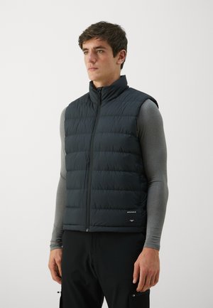 Black puffy vest with a stand-up collar, featuring a front zipper and horizontal stitching. Paired with a fitted gray long-sleeve shirt.