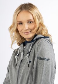Felpa grigia con zip, dal texture spazzolato, dettagli blu navy e lacci bianchi. Presenta un logo ricamato sulla manica e sul cappuccio.