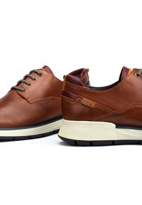 Zapatos de cuero marrón con diseño perforado, cordones grises, acentos burdeos y una suela intermedia blanca. Presenta una suela texturizada antideslizante y detalle del logo.