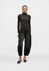 Schwarzes langärmliges Rollkragenoberteil kombiniert mit locker sitzenden, ausgewaschen schwarzen Jeans und schwarzen Ballerinas. Glatte Textur mit einer figurbetonten Silhouette.