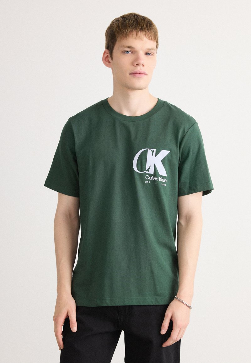 Grøn bomulds T-shirt med et hvidt Calvin Klein-logo på brystet. Korte ærmer og klassisk rund halsudskæring. Enkel design.