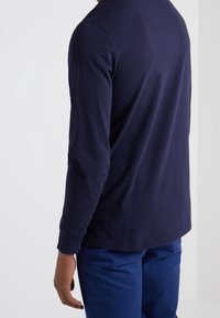 Maglietta a maniche lunghe color navy con scollo rotondo, in morbido cotone e vestibilità rilassata. Abbinata a pantaloni blu e un design semplice e minimalista.