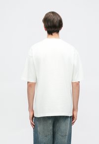 Biela bavlnená tričko s krátkymi rukávmi, vo voľnom strihu a s rovnomernejšími okrajmi. Jednoduchý dizajn, bez viditeľných vzorov alebo grafiky.