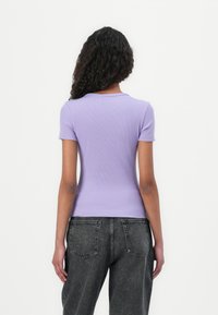 Haut à manches courtes en lin violet côtelé avec un col rond, associé à un jean taille haute gris foncé. Le tissu a une texture lisse.