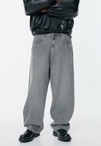 Graue Jeans aus Denim mit weitem Bein und leicht verwaschenem Muster, ausgestattet mit hoher Taille, Fünf-Taschen-Design und dekorativen Nähten.