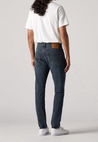 Mörkblå denim jeans med rak passform, läderbakfickpatch, subtila sömmar och en klassisk femficksdesign. Matcher med en vit t-shirt.