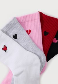 Quatre paires de chaussettes côtelées en blanc, gris, rose, rouge et noir, chacune ornée d'un petit cœur brodé de styles et couleurs différentes.