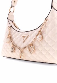 Borsa a spalla trapuntata beige con accenti dorati, dettaglio a catena e charm decorativi tra cui un fiore, un cuore e un lucchetto. Presenta una placca con logo.