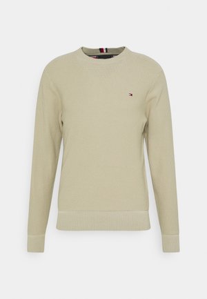 Beige langærmet striktrøje med rund halsudskæring og lille broderet rødt, hvidt og blåt logo på venstre bryst.