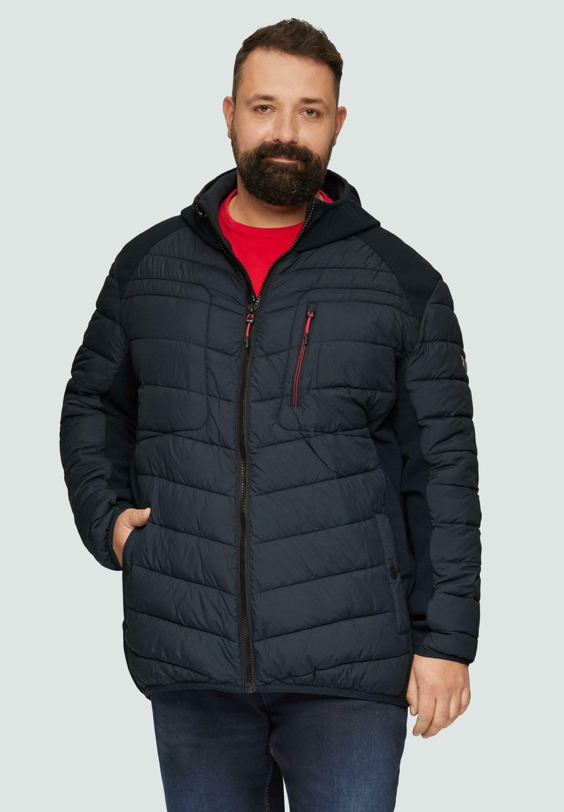 Granatowa kurtka puchowa z kapturem, pikowana tekstura, czerwone akcenty na zamku, boczne kieszenie i kontrastowe panele na ramionach. Nosi się ją na czerwonej koszuli.