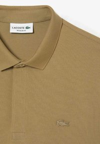 Khaki polo tričko s texturovanou tkaninou, s límcem na knoflíky a vyšitým logem Lacoste v odpovídající barvě na levém prsu.