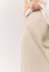 Beige satinkjol med en mjuk textur, som har en enkel och elegant design. Tyget faller mjukt och markeras av en ljusfärgad topp.