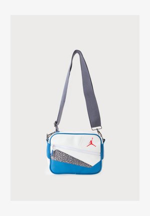 Mała prostokątna torba na ramię w kolorze białym i niebieskim z szarym regulowanym paskiem i czerwonym logo Jumpman na przedniej kieszeni.
