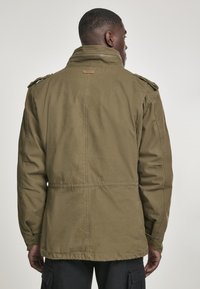 Olive green military-style jacket made of sturdy cotton, featuring shoulder epaulets, a high collar, and a straight cut.