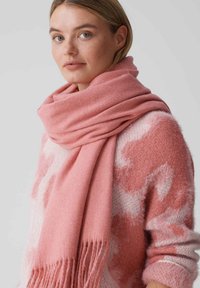 Roze sjaal gemaakt van zachte stof, met een gladde textuur en franjes aan de uiteinden. Draagt over een lichtroze en wit geblokte trui.