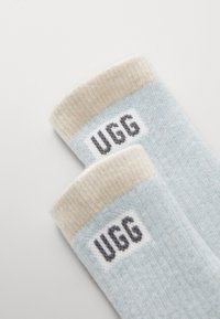 Calze di cotone azzurre chiare con un bordo a costine beige; presenta il logo "UGG" in grigio su una patch bianca vicino al bordo. Texture morbida.