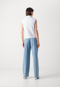 Colete acolchoado branco sem mangas com padrão em diamante, combinado com jeans de ganga azul-claro de perna larga, apresentando um corte descontraído e detalhes mínimos.