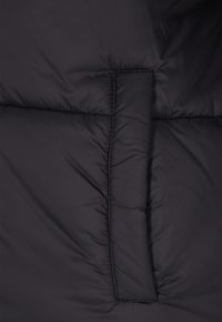 Fekete pufi dzseki anyag, mely varrott szakaszokkal rendelkezik a szigetelés érdekében. Simább textúra, enyhén fénylő felülettel. Nincs látható fémrész.