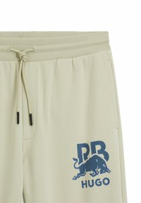Lichtbeige sweatpants met een elastische tailleband, een trekkoord, zijzakken en een blauwe grafische print met een stier en de initialen "PB HUGO."