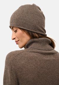 Brun stickad mössa med uppvikt kant, i kombination med en matchande polotröja. Båda plaggen har en mjuk textur och en enkel design.