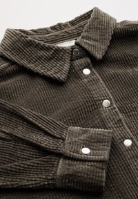 Camisa de pana marrón con cuello, botones de presión blancos y textura acanalada, de manga larga y corte relajado.