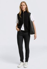 Črna rebrasta telovnik z visokim ovratnikom in sprednjo zadrgo, nošen prek bele majice s kratkimi rokavi. Združeno s črnimi hlačami in belimi supergami.