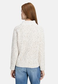 Chunky cream sweater with a high neck, textured knit pattern, and a relaxed fit. Styled with light blue jeans, shown from the back.