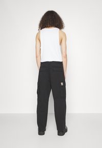 Mustat cargo-housut, joissa on useita taskuja ja rento istuvuus, yhdistettynä valkoiseen hihattomaan paitaaan, nähtynä takaa. Sujuva rakenne.