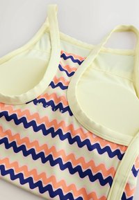 Haut de sport sans manches avec bretelles jaune clair, poitrine rembourrée et motif ondulé en zigzag rose, bleu marine et jaune clair.