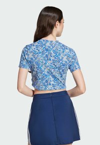 Blue floral crop top with short sleeves, featuring a mixed pattern. Paired with a navy skirt with side stripes and a zip closure.
