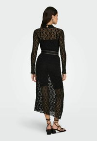 Černé krajkové šaty s dlouhými rukávy, vysokým výstřihem a poloprůhlednou sukní s bočním rozparkem. Doplněné páskem s cvočky.