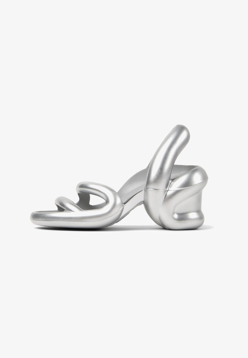 Sandal de salto alto prateada com um design escultural, acabamento metálico suave e um detalhe de tira torcida único na parte da frente.