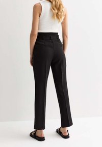 Zwarte op maat gemaakte broeken met een rechte snit, hoge taille en riemlussen, gecombineerd met een witte geribbelde tanktop en zwarte sandaal. Glad textuur.