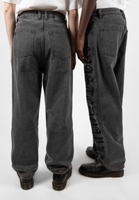 Grå denimvidbyxor med medelhög midja, med bakfickor och stora svarta grafiska bokstäver längs sidan.