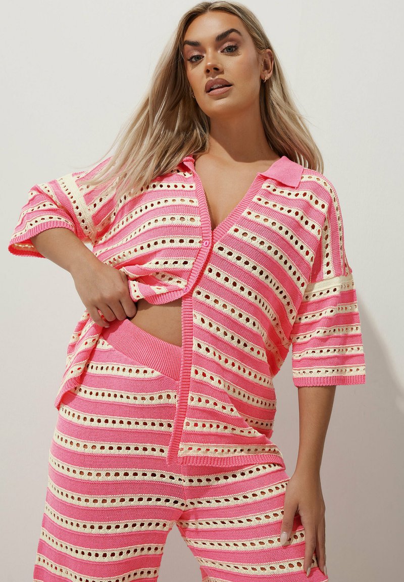 Completo di abbigliamento per il tempo libero lavorato a maglia, caratterizzato da un motivo a righe rosa e crema con dettagli a traforato. La parte superiore ha una scollatura a V e maniche corte, mentre i pantaloni sono aderenti.