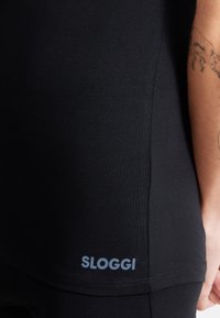 Black Sloggi garment features a smooth, stretchy fabric with a fitted design. It includes a subtle logo near the hem and textured seam details.