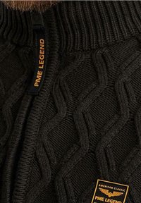 Pull en maille vert foncé avec un col montant, présentant un motif torsadé, et une étiquette de la marque PME Legend cousue sur la poitrine.
