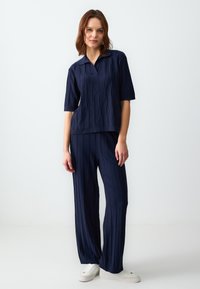 Maglietta navy a maglia con colletto e maniche corte, abbinata a pantaloni a gamba larga a coste. Entrambi presentano un motivo a righe verticali.