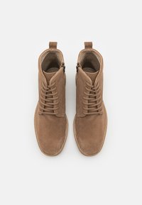 Botas de tobillo de ante marrón con punta redondeada, diseño de cordones y detalles de cremallera en los laterales. Presenta una suela de goma cosida.
