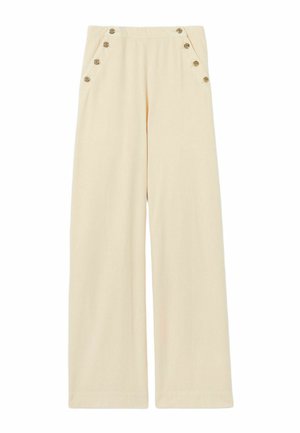 Femme portant un haut sans manches rayé bleu marine et blanc avec un ourlet froncé, un pantalon large crème taille haute avec des boutons et des chaussures marron.