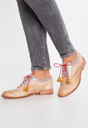 Zapatos con cordones que cuentan con una parte superior de cuero de color claro con acentos plateados, perforaciones amarillas y cordones rojos, adornados con borlas amarillas.