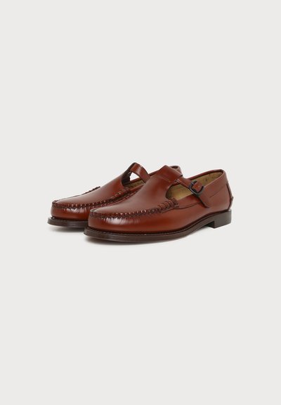 Mocassins pour hommes en cuir marron avec une bride et une boucle, détails cousus et talons bas, présentés côte à côte sur un fond uni.