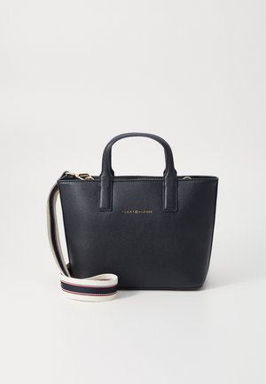 Navy blue leather handbag with two short handles and a detachable shoulder strap. Gold logo on the front. Smooth texture, structured design.