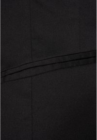 Gros plan sur un tissu noir avec des coutures diagonales et verticales visibles, et un détail plié horizontalement au centre.