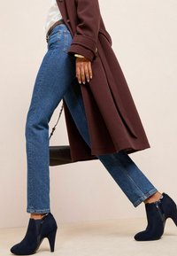 Vaqueros de mezclilla azules, abrigo marrón y botines negros con cremallera. Los vaqueros son de corte clásico y el abrigo presenta un diseño entallado.