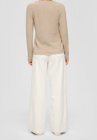 Pull beige en maille à manches longues et col rond, associé à un pantalon blanc à jambes larges. Palette de couleurs simple et neutre.