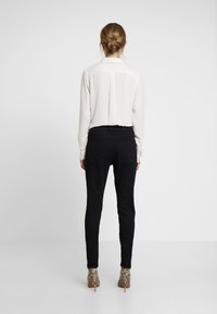 Light beige long-sleeve blouse with a pleated back, paired with black fitted pants and snake-patterned high-heeled ankle boots.