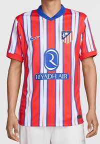 Punainen ja valkoinen raidallinen jalkapallopaita, jossa on sininen kaulus. Paidassa on Nike-logo, seuramerkki ja sponsorin nimi sinisellä rinnassa. Valmistettu teksturoidusta kankaasta.